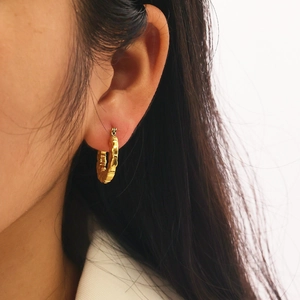Close-up of gold hollow hoop earrings with bamboo texture on a model wearing a white suit