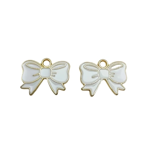 Detailed macro view of two white enamel bow pendants with gold metal edges for DIY jewelry