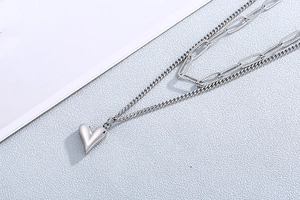 Détail d'un collier double épaisseur argenté avec pendentif coeur et maillons trombone