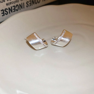 Macro shot of silver layered ribbon earrings with micro-set zircons on ceramic plate