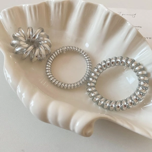 Close-up of metallic silver spiral hair ties displayed in a white decorative shell tray