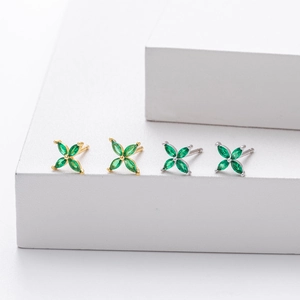 Detail of four-leaf clover stud earrings in gold and silver finish with green stones