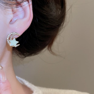 Detail of elegant gold crescent moon and star earrings with pavé zircons on ear