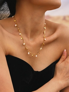 Detail of gold shell and teardrop pearl necklace worn by a model in warm light