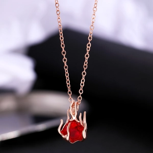 Macro shot of a rose gold necklace featuring a flame-shaped pendant with a red gemstone