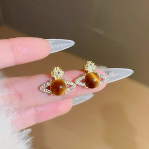 Detailed close-up of gold saturn planet earrings with cat eye stone and white zircons