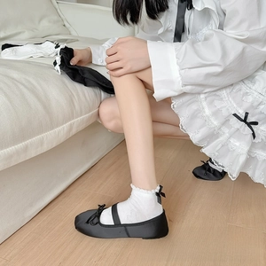 Close-up of white Lolita socks with lace ruffles and black bow details on a model