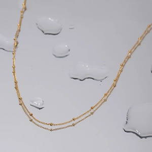 Collier double couche doré à perles étanche au design minimaliste sur fond miroir avec eau