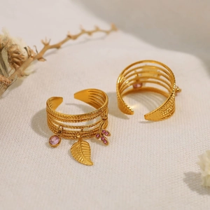 Gold multi-layer stainless steel ring with pink gemstone and leaf pendant on white fabric