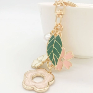 Detail of gold keychain with enamel green leaf, pink flower and sparkling rhinestones