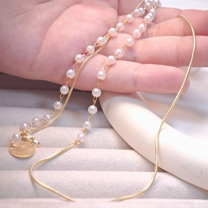 Detail of double-layer pearl necklace with gold snake chain and round pendant held in hand