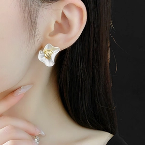 Close-up of elegant white floral stud earrings with gold center worn by a model