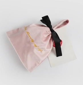 Details einer rosa Samt-Geschenktüte mit schwarzer Satinschleife und Goldstickerei