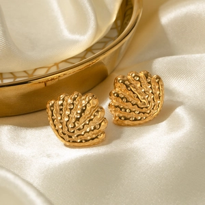 Detailed view of golden shell earrings on white silk fabric with luxury wave texture