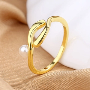 Macro shot of polished gold-tone twisted ring with a white pearl on silk fabric