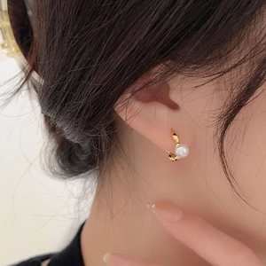 Close-up of a model wearing gold pearl hoop earrings with minimalist olive branch design