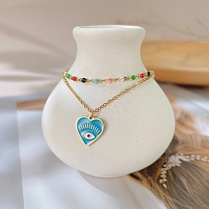 Detail of layered gold bracelet featuring blue enamel heart and devil eye charm decoration