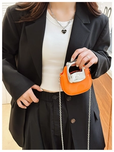 Close-up of a mini orange crossbody bag with silver chain and heart-shaped Forever necklace