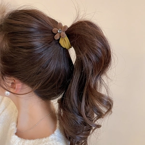 Détail d'un élastique avec fleur floquée marron et strass porté sur une queue de cheval