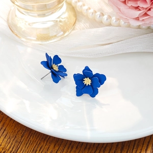 Macro detail of blue matte flower earrings with yellow centers on a ceramic plate