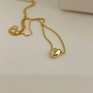 Detailed view of a gold heart pendant on a delicate box chain against white background