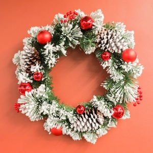 Christmas wreath with snowy pine needles, red berries, and natural pine cones on red backdrop