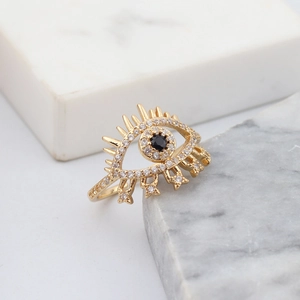 Close-up of golden evil eye ring with black stone and crystals on marble stone
