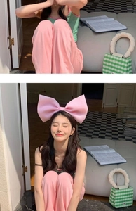Detail showing an oversized pink bow headband worn by a model in a cozy, bright room