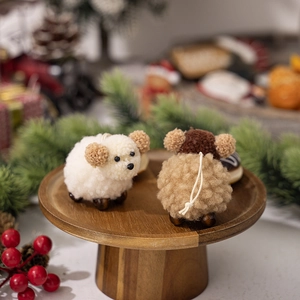 Close-up of plush wool felt sheep ornaments with wooden bead legs on a festive wooden tray