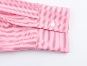 Dettaglio della manica di una camicia a righe rosa con bottone bianco e cuciture fini