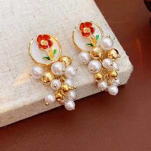 Vue macro de boucles d'oreilles fleurs en émail et perles sur tissu beige texturé