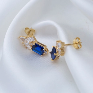 Close-up of luxury gold earrings with blue rectangular gemstone on white silk