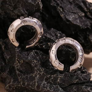 Macro shot of silver heart-patterned ear cuffs displayed on a dark textured rock surface