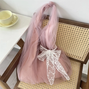 Détail d'un sac cabas en tulle rose avec un grand nœud en dentelle blanche sur une chaise