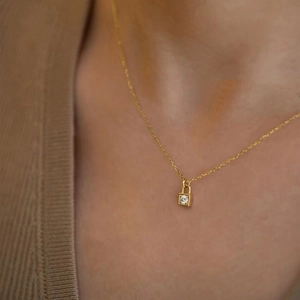 Close-up of a gold lock pendant necklace with a single diamond worn on a woman neck