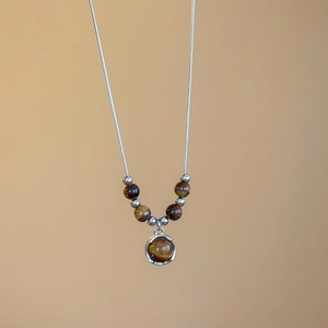 Macro detail of tiger eye stone pendant necklace with brown beads and snake chain