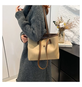 Detail of soft beige tote bag with brown handles worn on shoulder by model