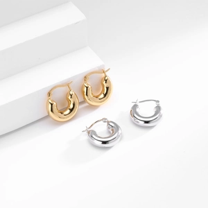 Detailed close-up of polished silver and gold hoop earrings on minimalist display stand