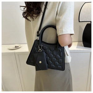 Detailed view of a black quilted shoulder bag with embossed patterns and small pouch