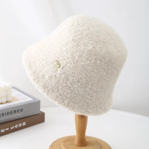 Close-up of a white lamb wool bucket hat on a wooden stand with minimalist decor.