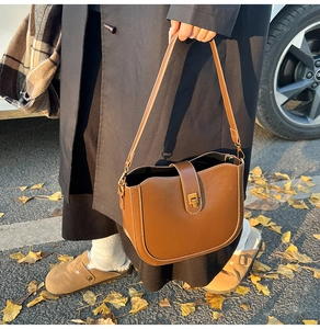 Brown leather saddle bag with golden buckle shown in a scenic autumn street setting