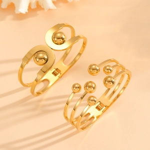 Macro view of two polished gold stainless steel open bangles with spherical accents
