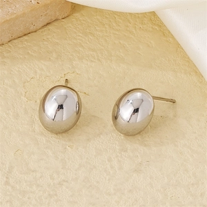 Macro shot of silver bean-shaped earrings on textured stone and white silk fabric