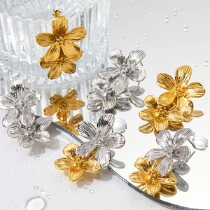 Blumen-Ohrringe aus Edelstahl in Gold und Silber auf einer reflektierenden Wasseroberfläche