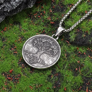 Close-up of silver steel Tree of Life pendant on a box chain set against mossy nature