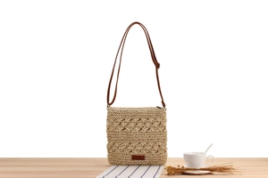 Close-up of beige hollow woven straw shoulder bag with brown leather strap and logo detail