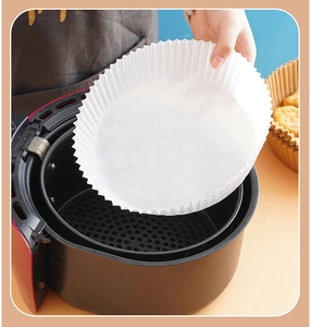 Detail showing a hand placing a round white silicone paper liner into an air fryer basket