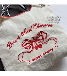 Detail of embroidered cherries and bows on off-white nylon fabric with woven rope handle