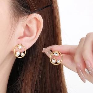 Minimalist gold hollow round studs with inset crystals for women displayed on ear and hand