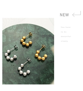 Detailed view of gold and silver beaded C-shaped stud earrings on green marble